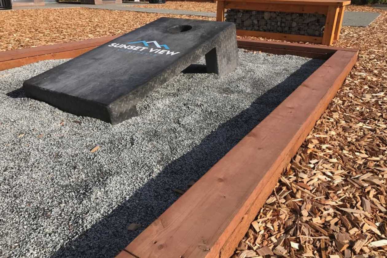 Concrete cornhole game in a landscaped outdoor area with a timber border