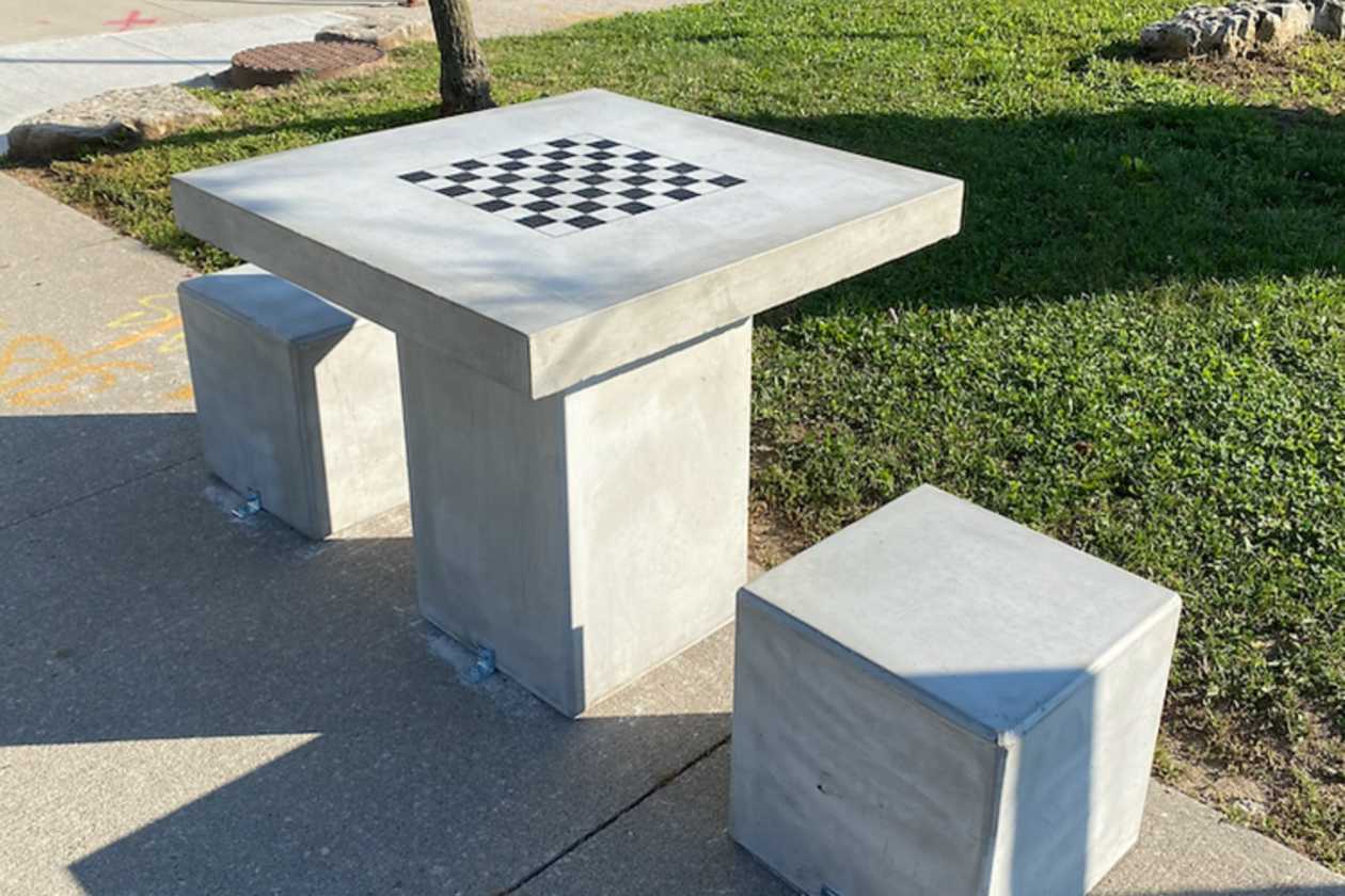 Concrete chess table and seats beside a lawn and planted border