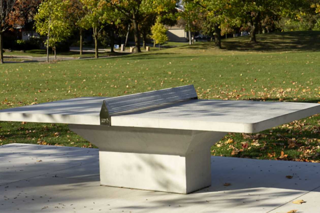 Outdoor ping pong table on a paved area surrounded by trees