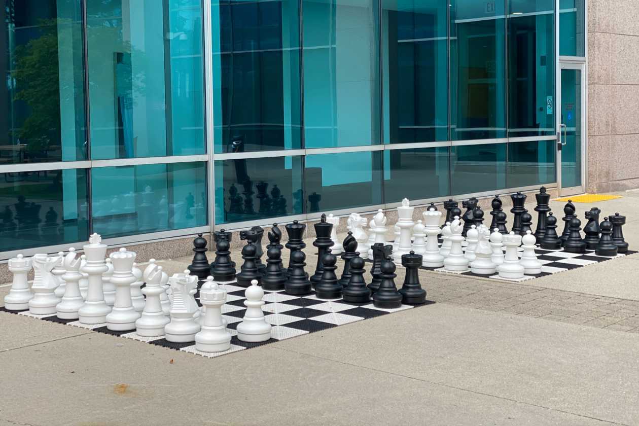 Giant chess set on paving outside a glass-fronted building